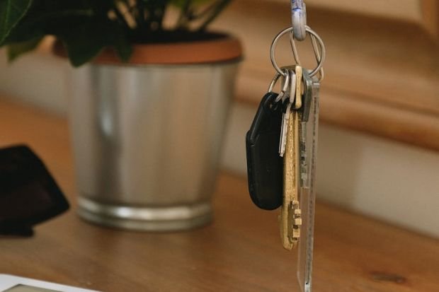 A close-up of a hand holding a set of keys above a tablet on a wooden table.