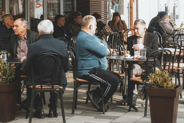 Senior men engaging in conversation at a bustling outdoor cafe on a city street.