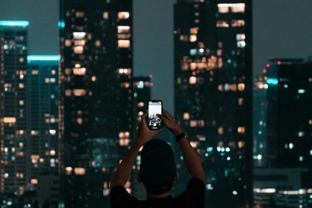 A person photographing Jakarta's illuminated skyscrapers during a vibrant city night.
