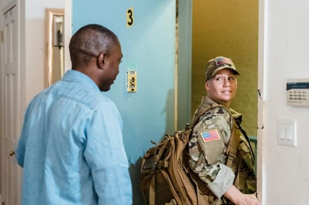 A soldier in uniform reunites with her partner at home, showcasing love and diversity.