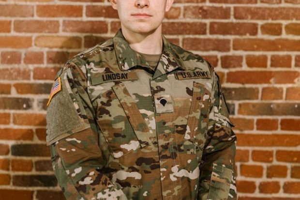 A proud US Army soldier in uniform stands against a brick wall, embodying patriotism and honor.